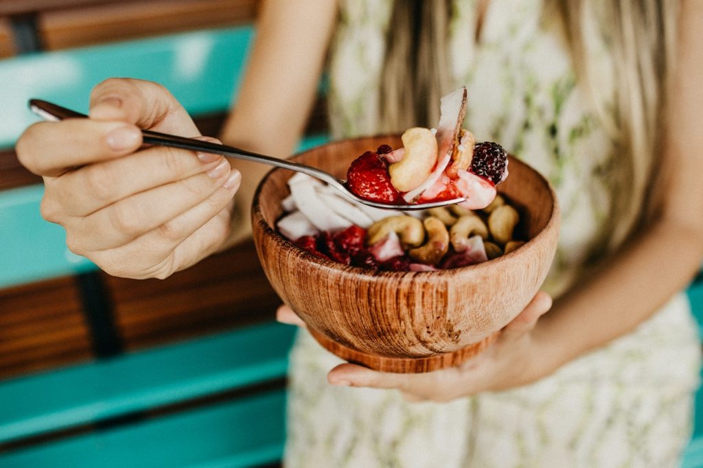 Woman eating a smoothie bowl with cashews, berries, and coconut.