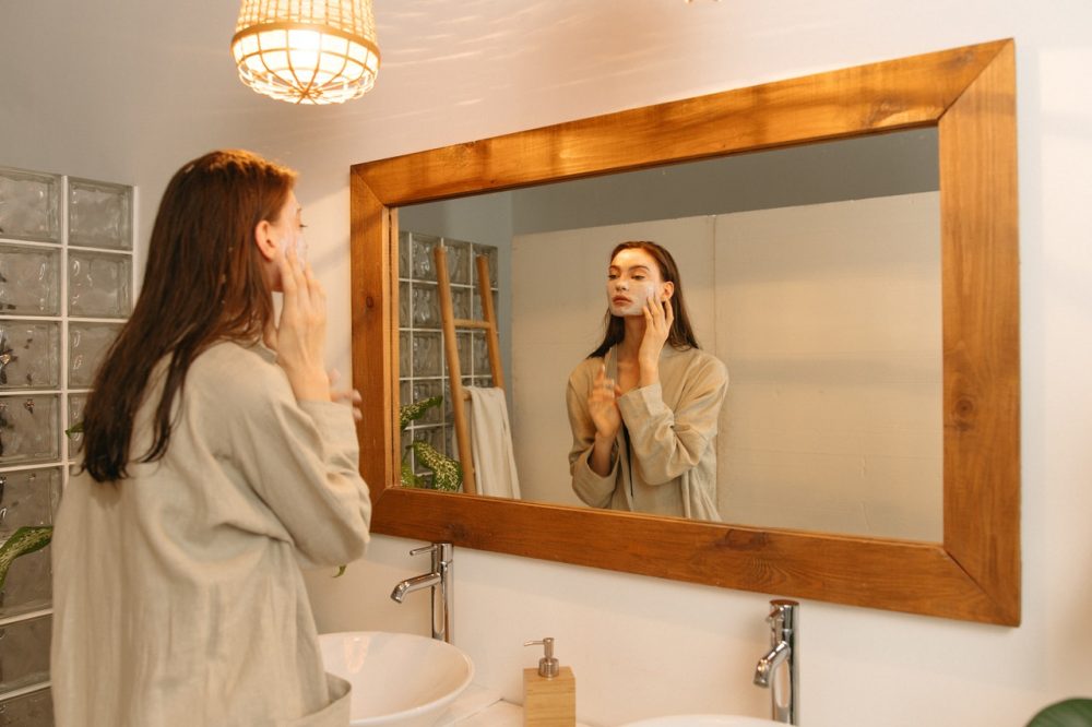 Woman Applying Cosmetic Product on Her Face While Looking at Mirror