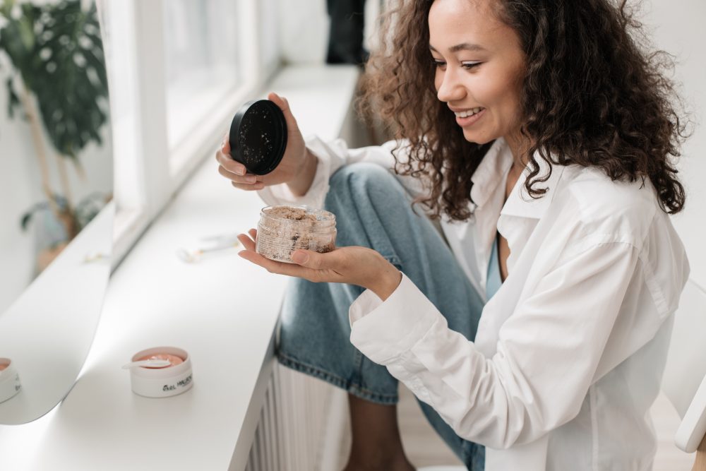 Woman opening up a body scrub while doing her makeup