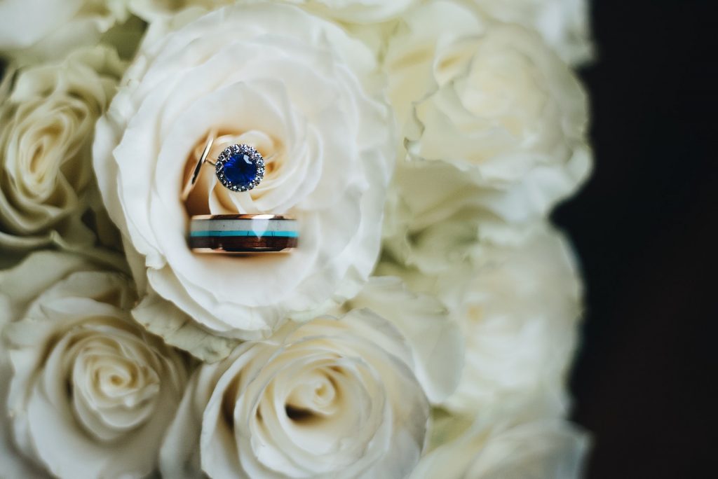 Sapphire engagement ring and a manly bands wedding band displayed in a white rose