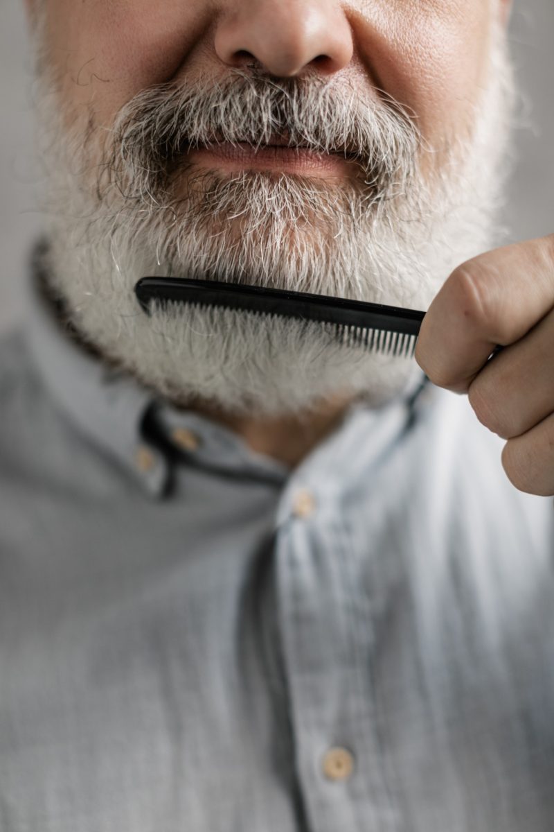 Man with grey hair brushing beard with comb
