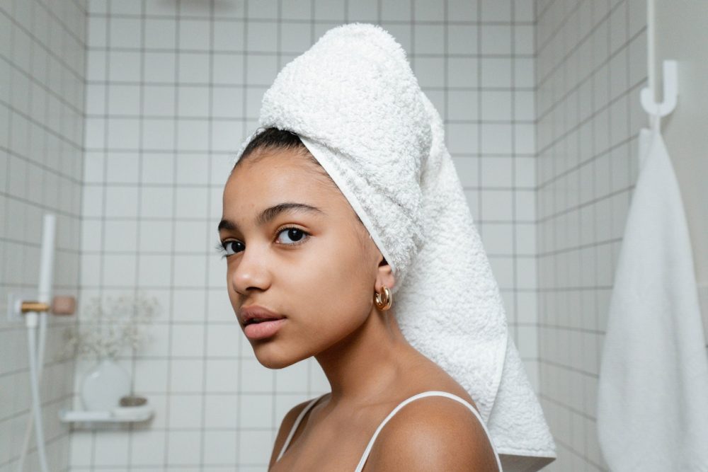 Woman with white towel on head looking in mirror during skincare routine