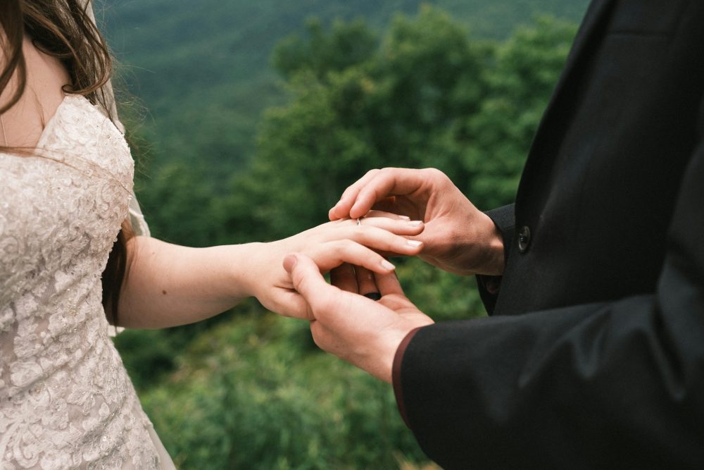 man putting engagement ring on woman's finger outside